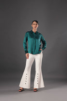 Woman wearing a green satin shirt and white flared pants on a gray background