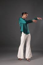 Woman in teal top and white pants posing against a gray background