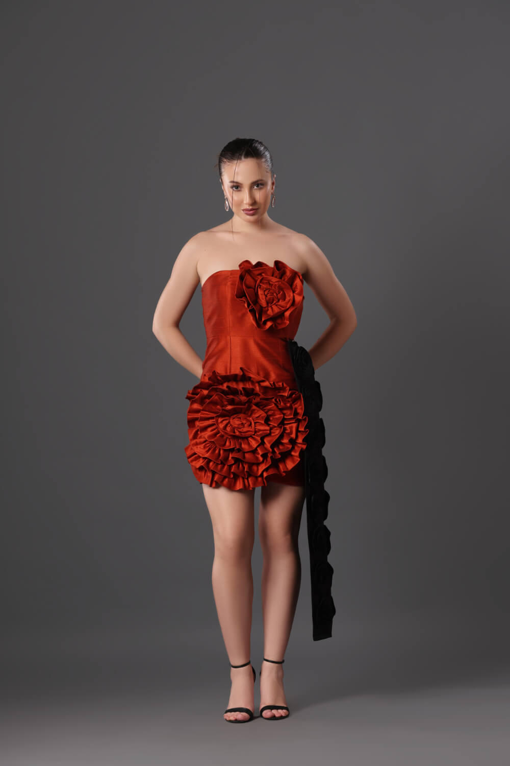 Woman wearing a strapless red dress with floral details on a gray background