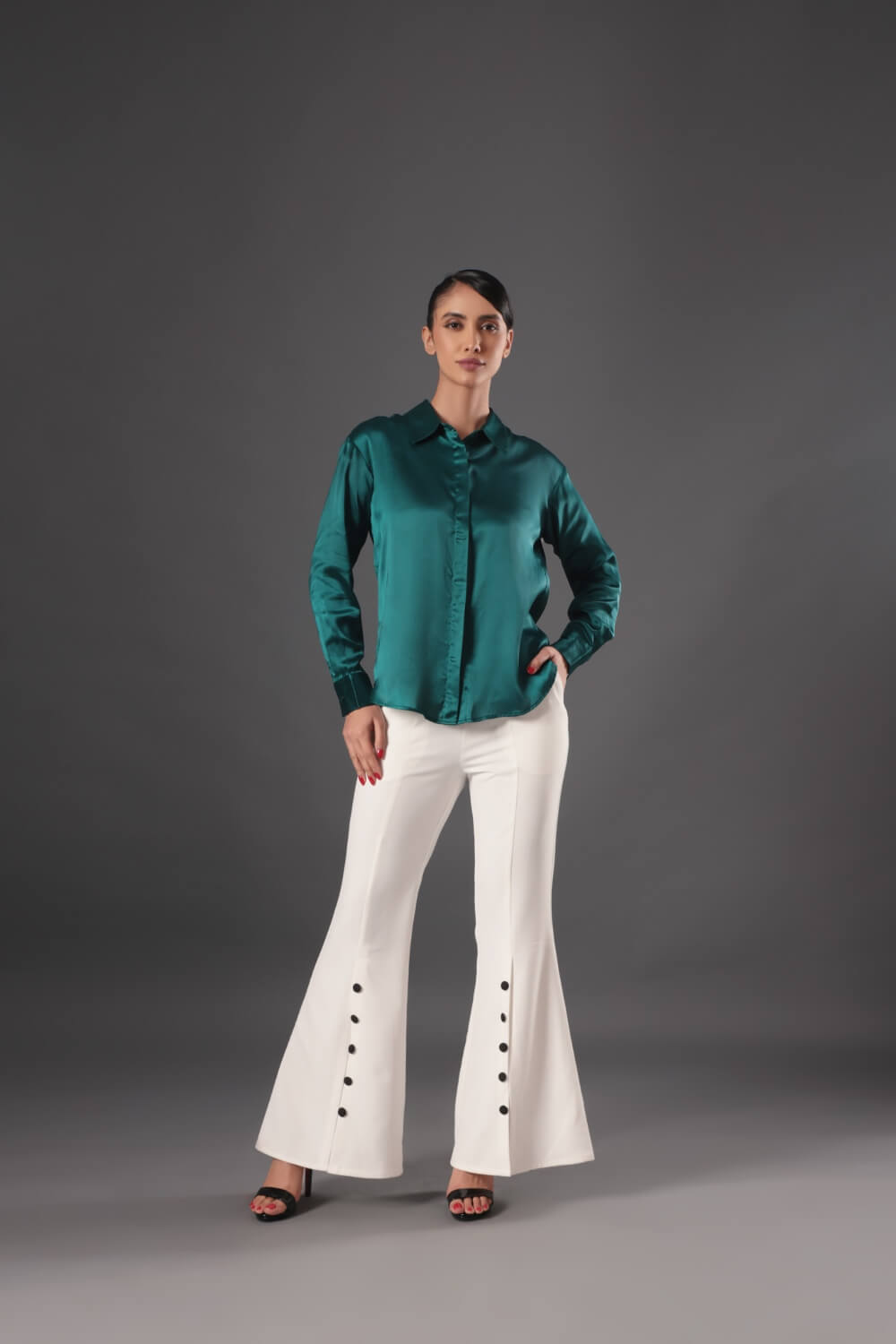 Woman wearing a green satin shirt and white flared pants on a gray background