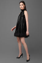 Woman wearing a black sequin dress with feather trim on a gray background