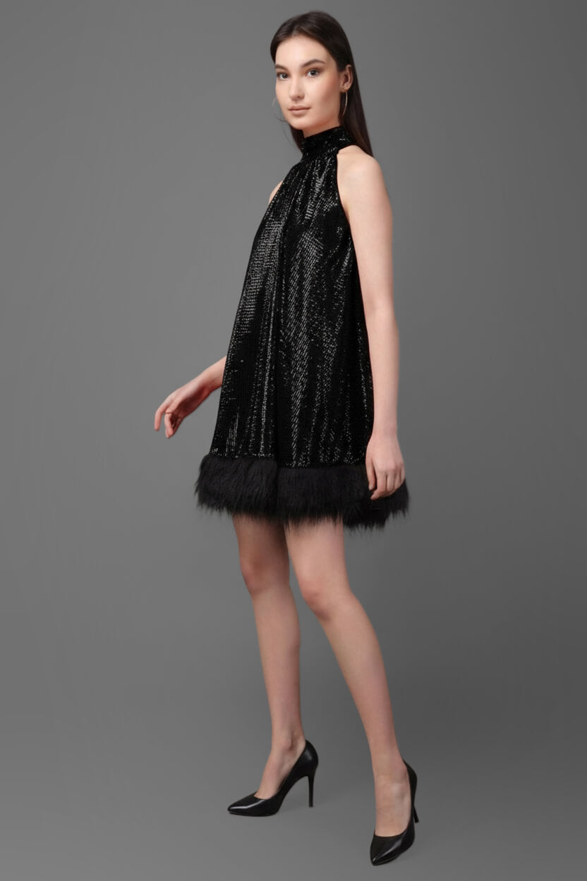 Woman wearing a black sequin dress with feather trim on a gray background