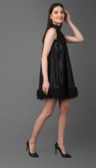 Woman wearing a black sequin dress with feather details on a gray background