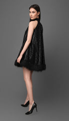 Woman wearing a black sequin dress with feather trim on a gray background