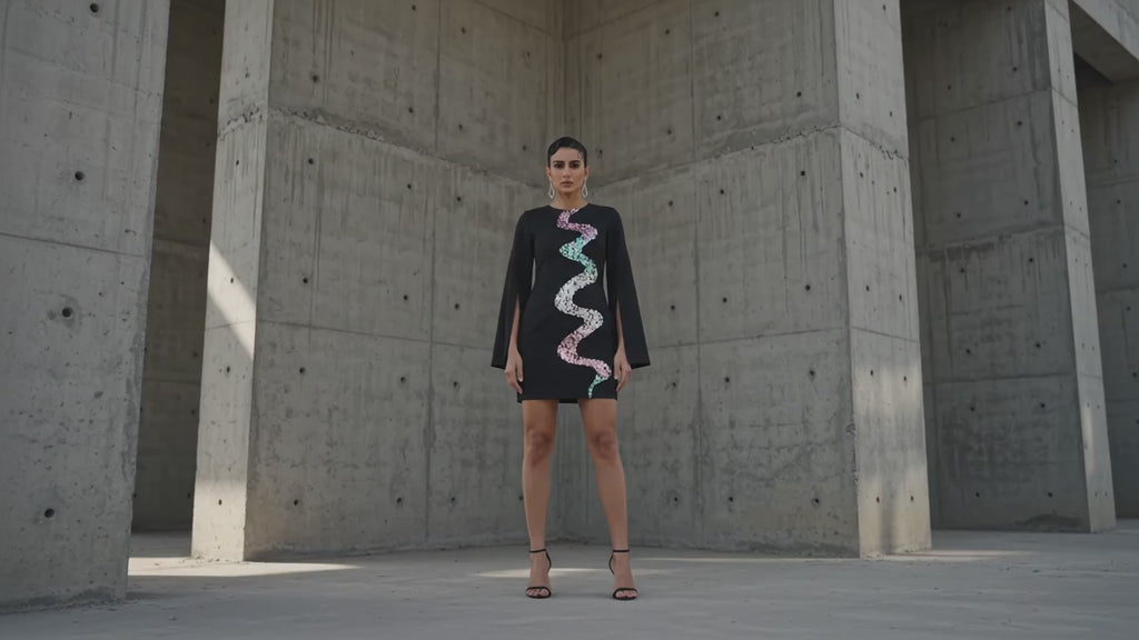 Woman wearing a black dress with colorful sequin patterns on a gray background