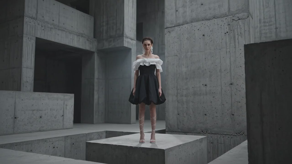 Woman in a black dress with white ruffled top in a concrete architectural setting