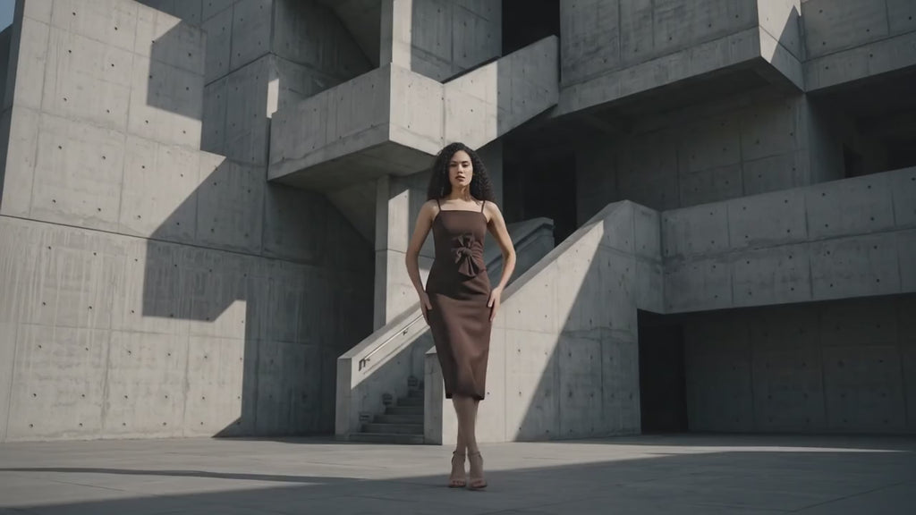 Woman in a brown dress standing against a textured wall.