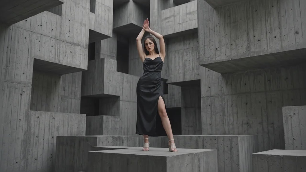 Woman in a black satin dress standing in a geometric, abstract architectural setting.